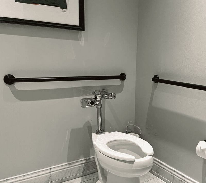 Matte black grab bars on grey tile in a commercial restroom